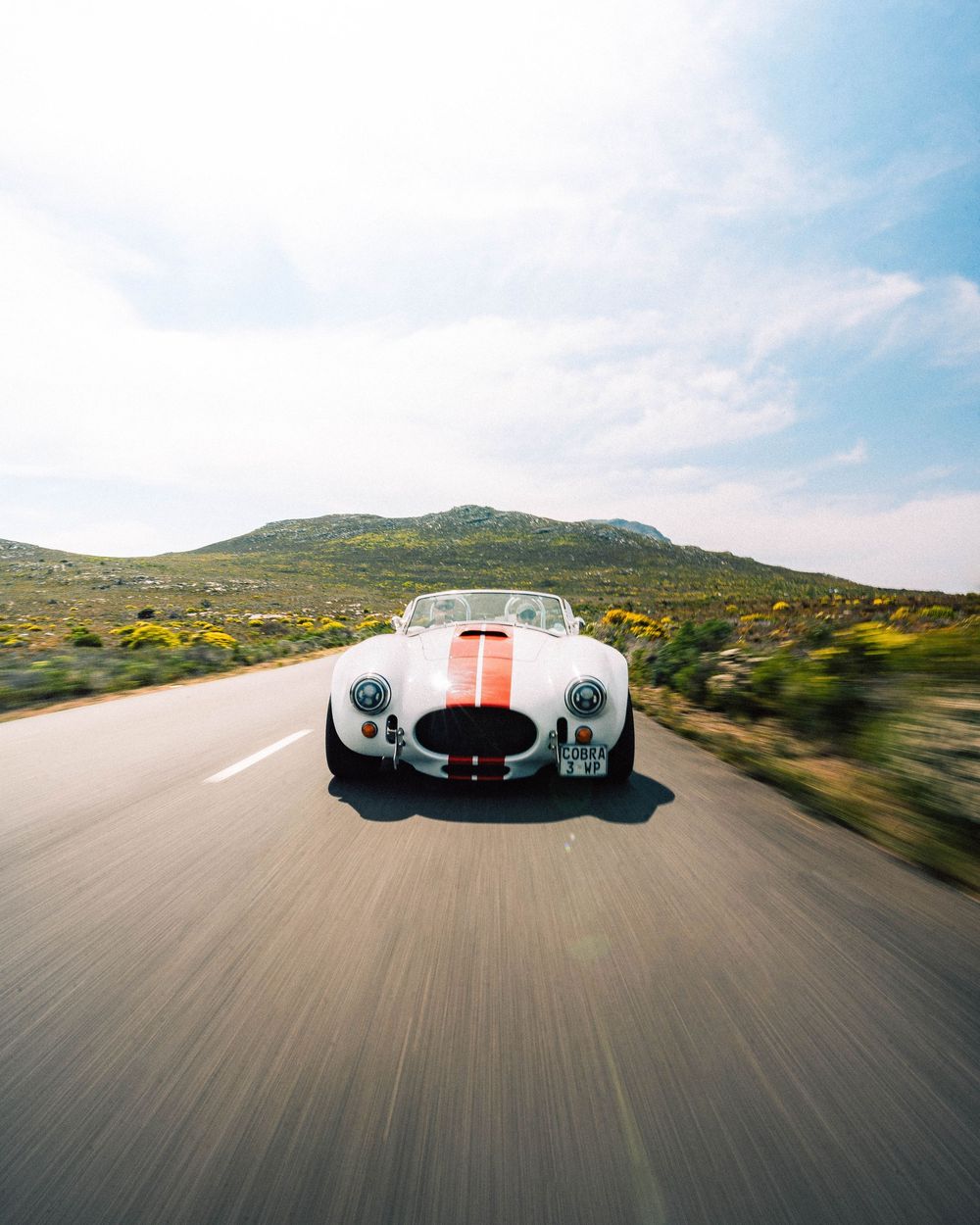 Classic vintage Porsche race car with white and orange paint scheme photographed in motion on a desert road.