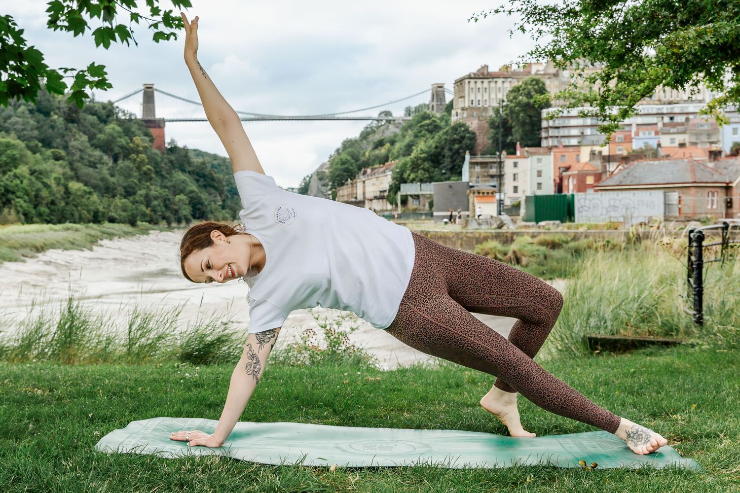 A yoga teacher smiles as she poses by the River Avon and Clifton Suspension Bridge. Natural website and brand photographer Bristol