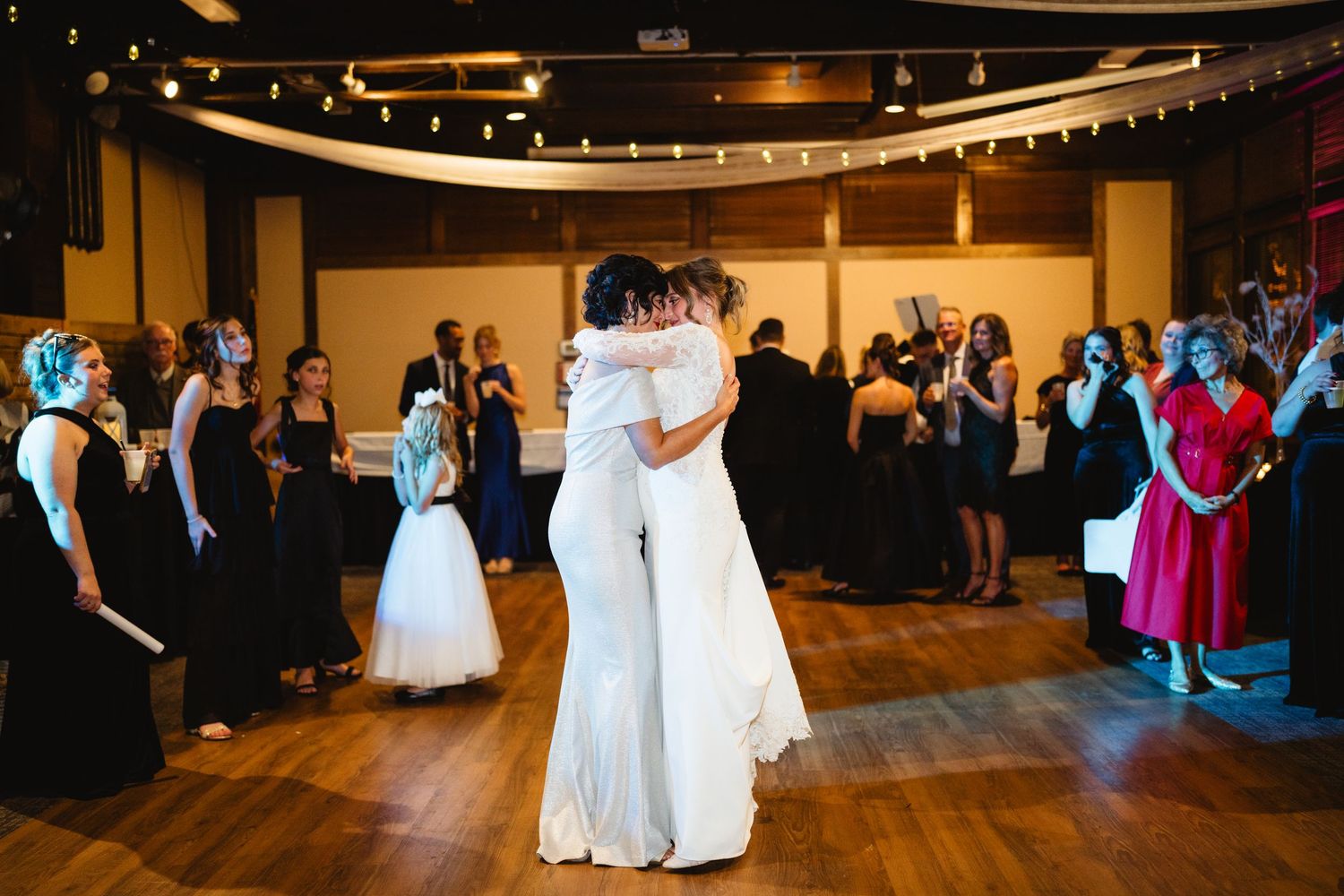 People dance together on a wooden floor under warm lighting during a wedding reception celebration.