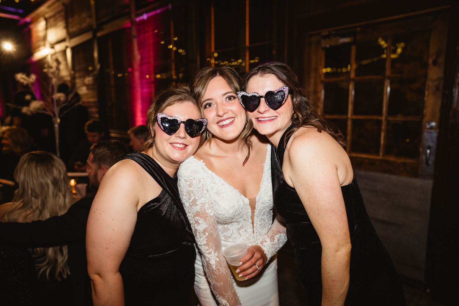 Wedding guests in sunglasses and formal attire pose together during an evening celebration.