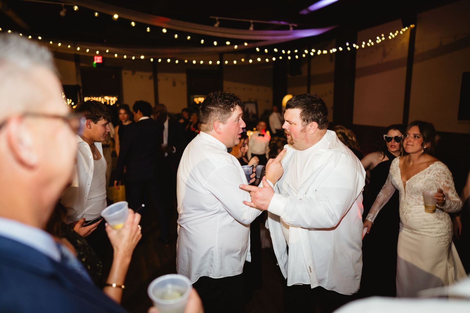 Guests in white attire dancing and celebrating at an elegant evening reception with string lights overhead.