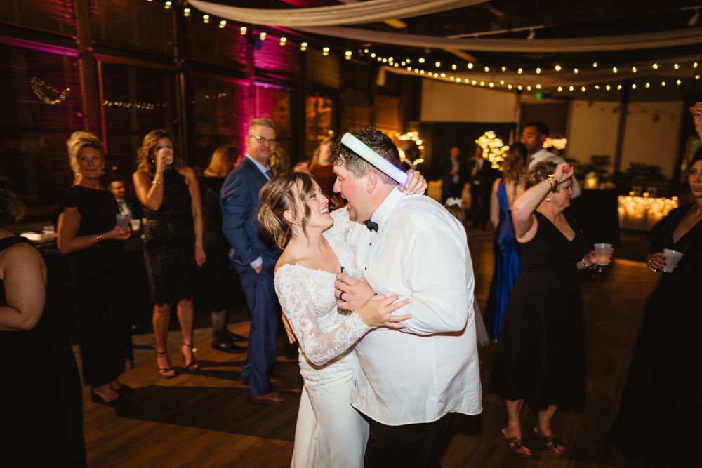 Couples slow dancing together at an evening reception with string lights and romantic lighting overhead.