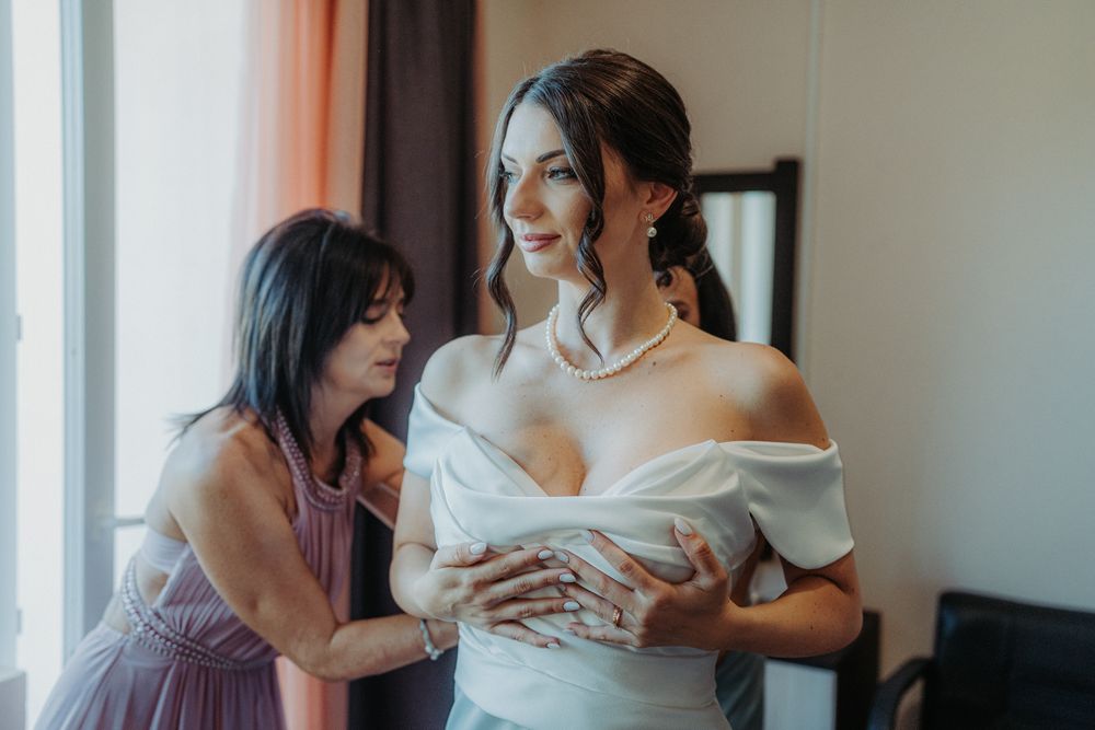 A tender moment between two people as they prepare for a wedding ceremony in a sunlit room.