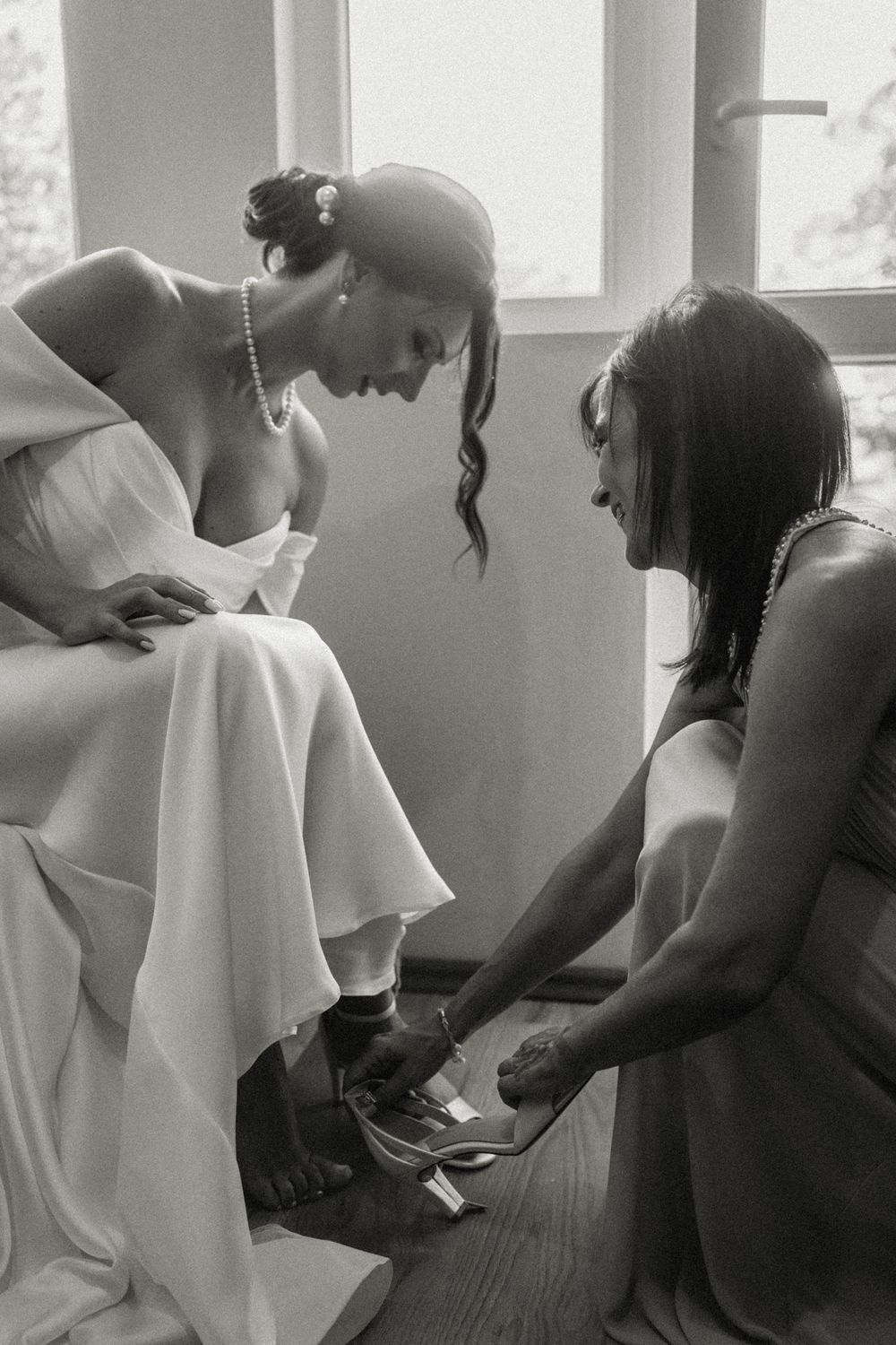 Black and white photo showing final wedding preparations as shoes are being adjusted.