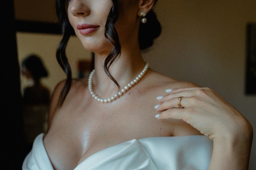 Close-up of bridal jewelry featuring pearl necklace and engagement ring with white dress.