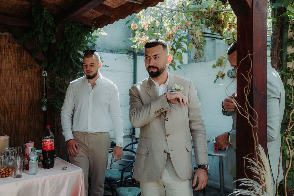 Two guests in light colored suits stand under a covered patio during an outdoor event.