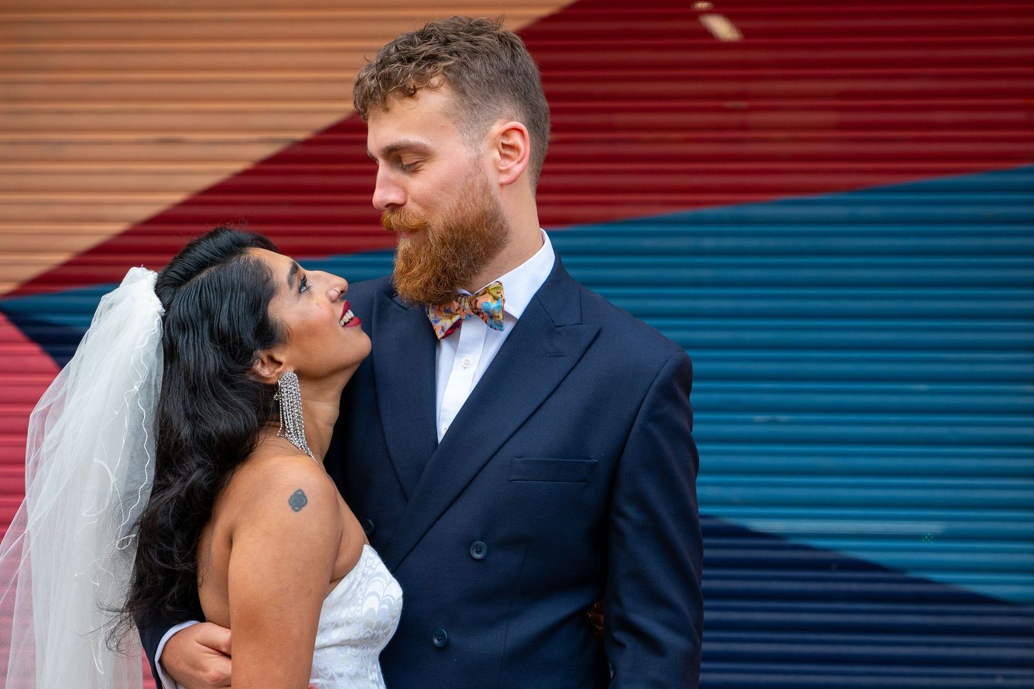 A bride and groom share intimate moments in front of colorful striped backgrounds during their wedding photoshoot.