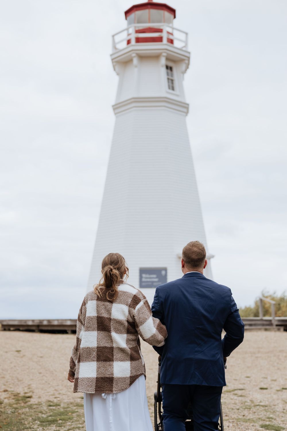 Bride and groom elope at Cape Jourimain Nature Centre infront of a light house and Confederation Bridge to PEI during cold October wedding