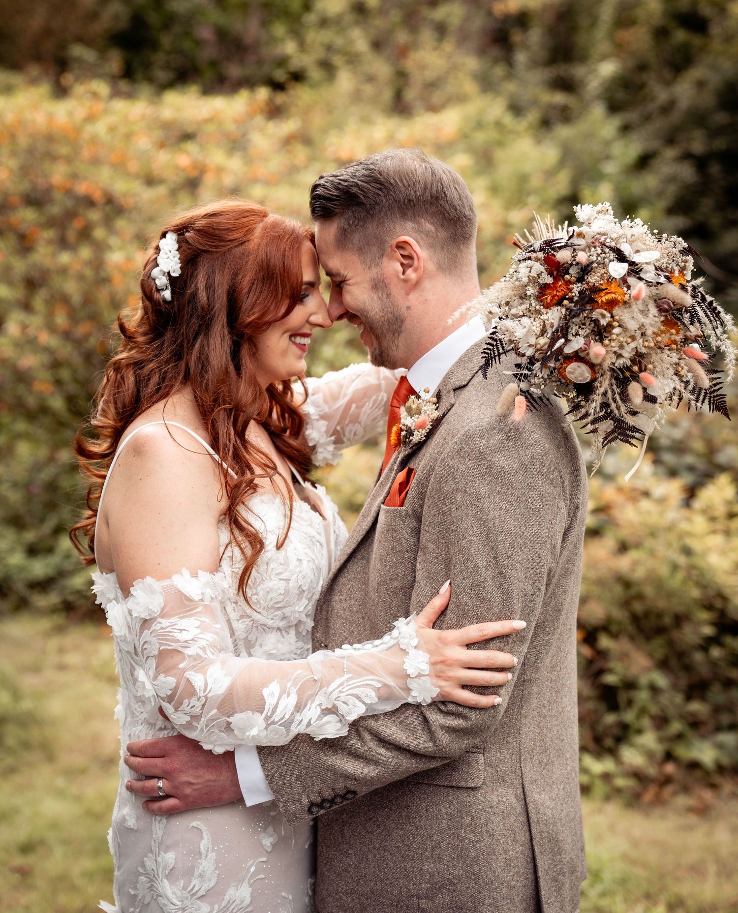 A romantic autumn wedding moment with a couple embracing outdoors, featuring a lace dress and tweed suit.
