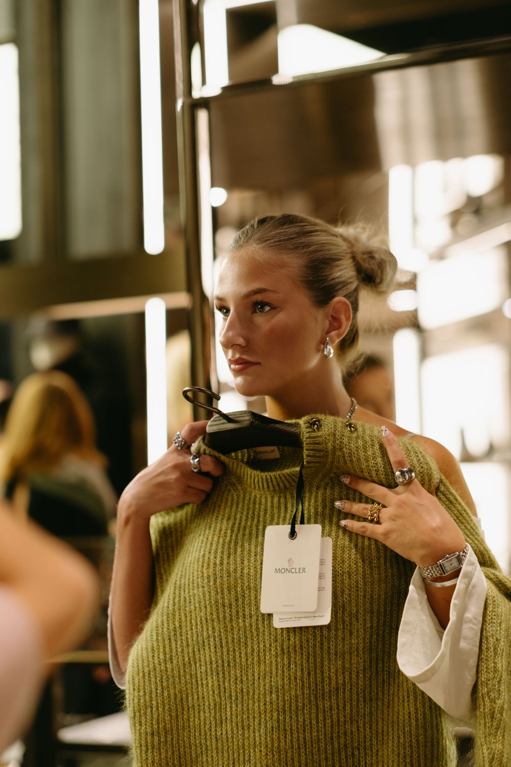 woman trying on a sweater looking in a mirror at luxurious brand store while being captured by the best event photographer in Stockholm