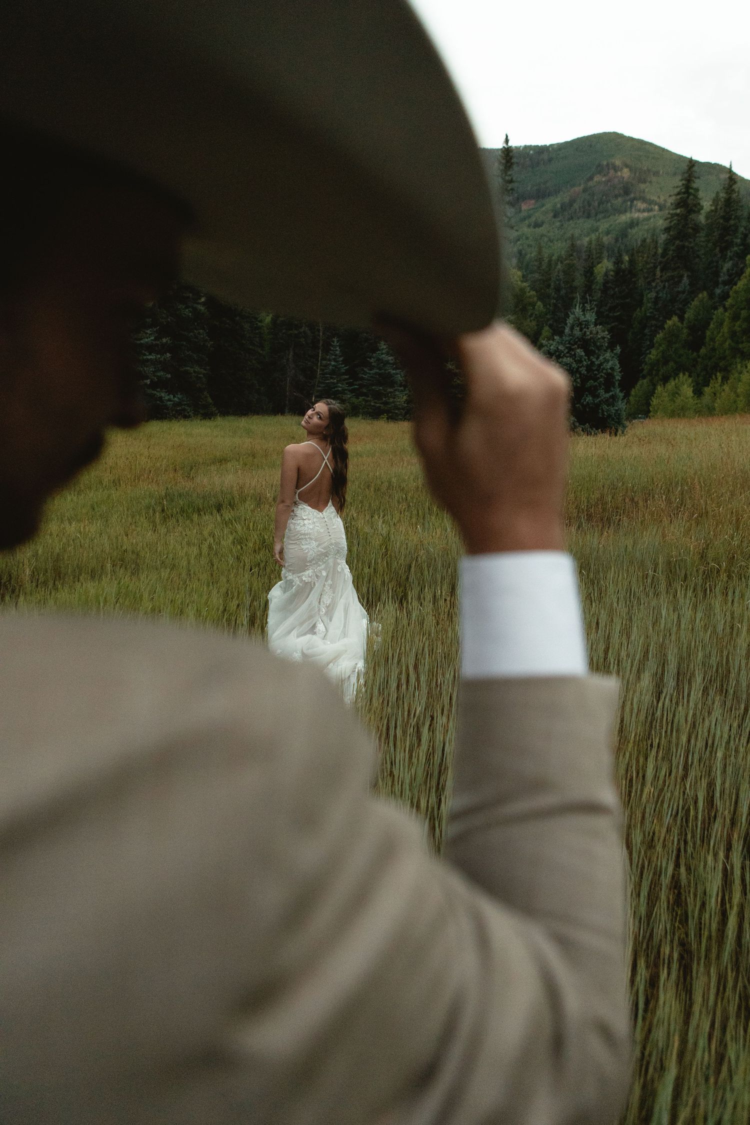 Groom tips his hat at bride in field