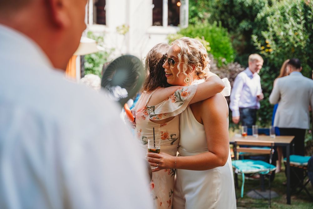 Wedding guests enjoying an outdoor celebration with drinks and laughter at a garden reception.