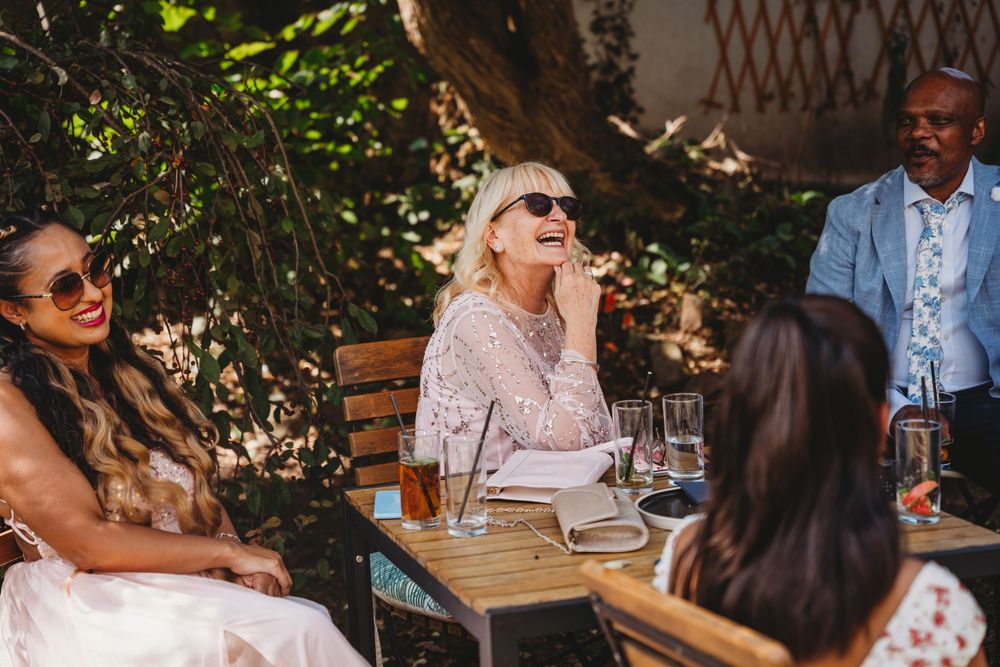 Guests mingling at an outdoor wedding reception under natural greenery and sunlight.