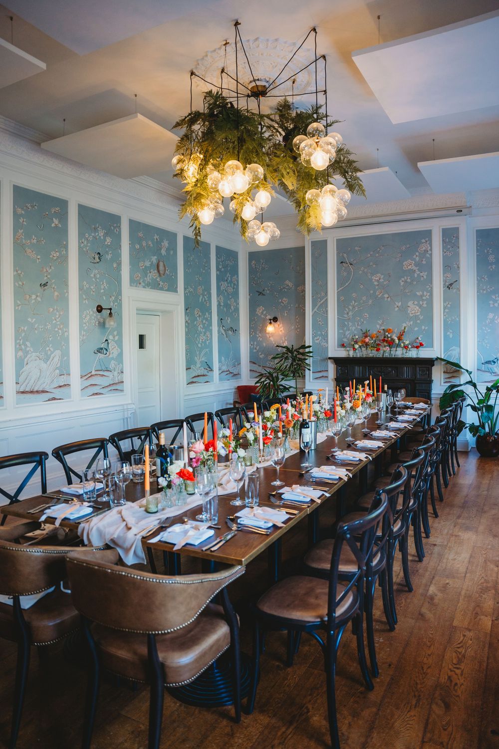 Elegant dining room with blue wallpaper and wooden tables set for a wedding reception.