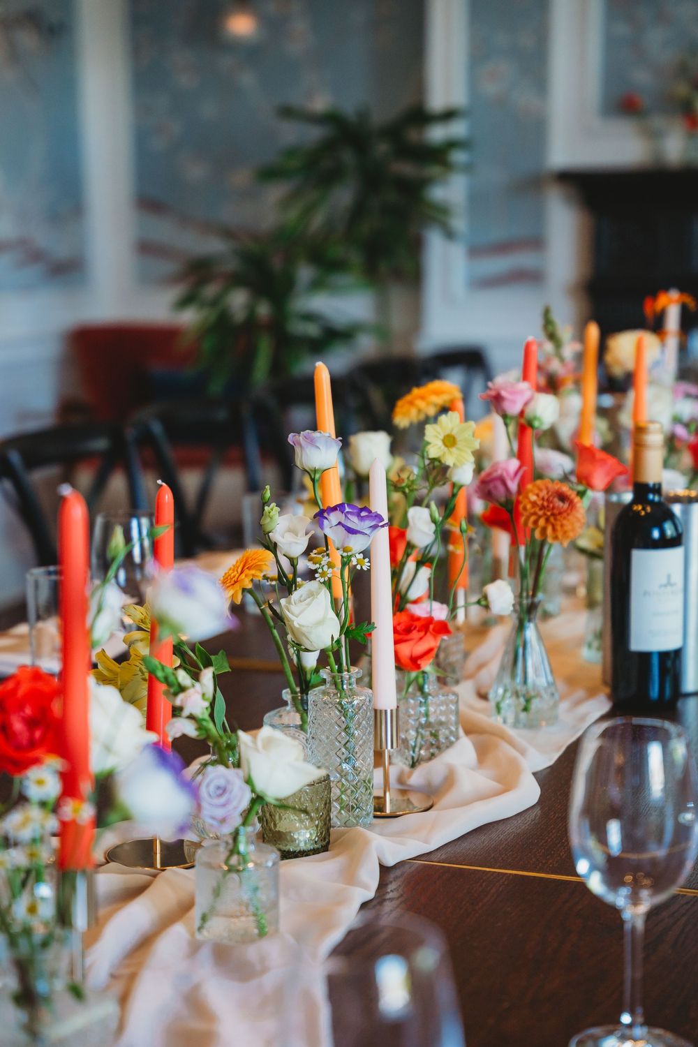 Beautifully decorated wedding table with colorful flowers in bud vases and red taper candles.