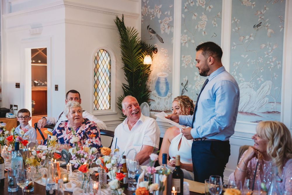 Wedding reception dining room filled with guests during emotional toasts and speeches.