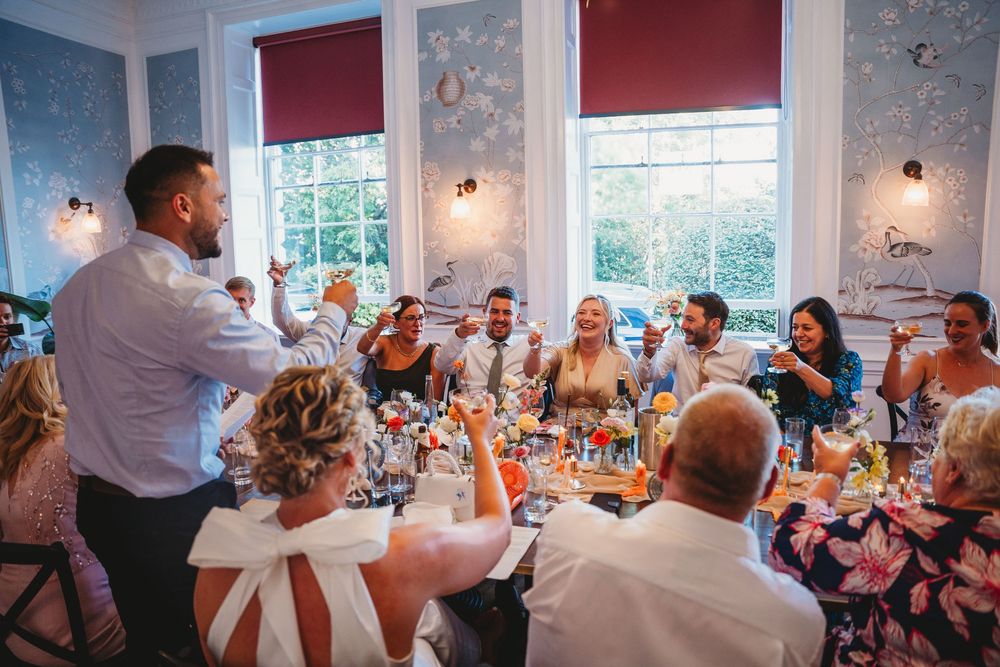 Wedding reception guests seated at decorated tables in a bright indoor venue with red accent walls.