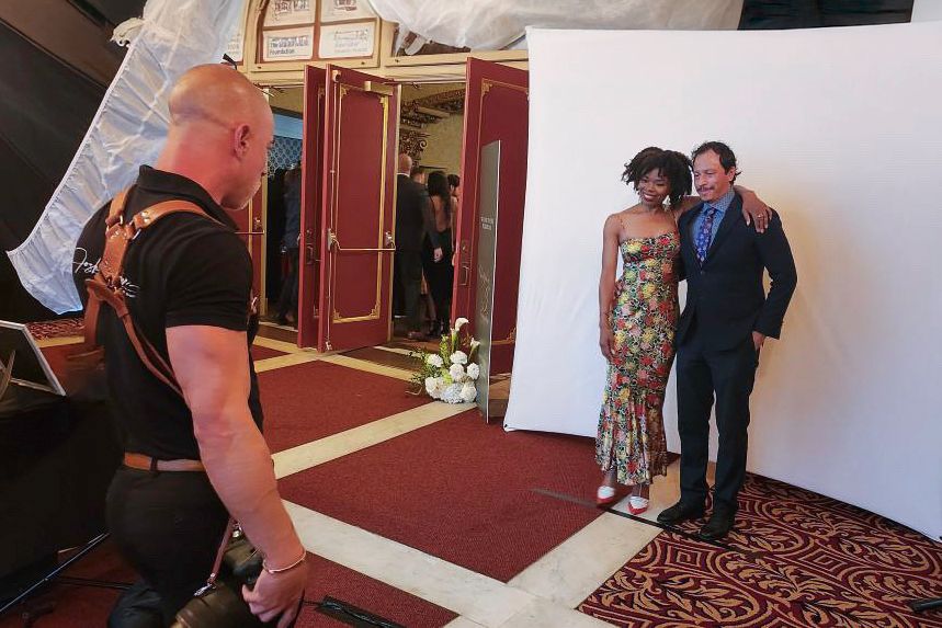 Professional photographer captures a couple posing against a white backdrop in an elegant venue with red carpet.