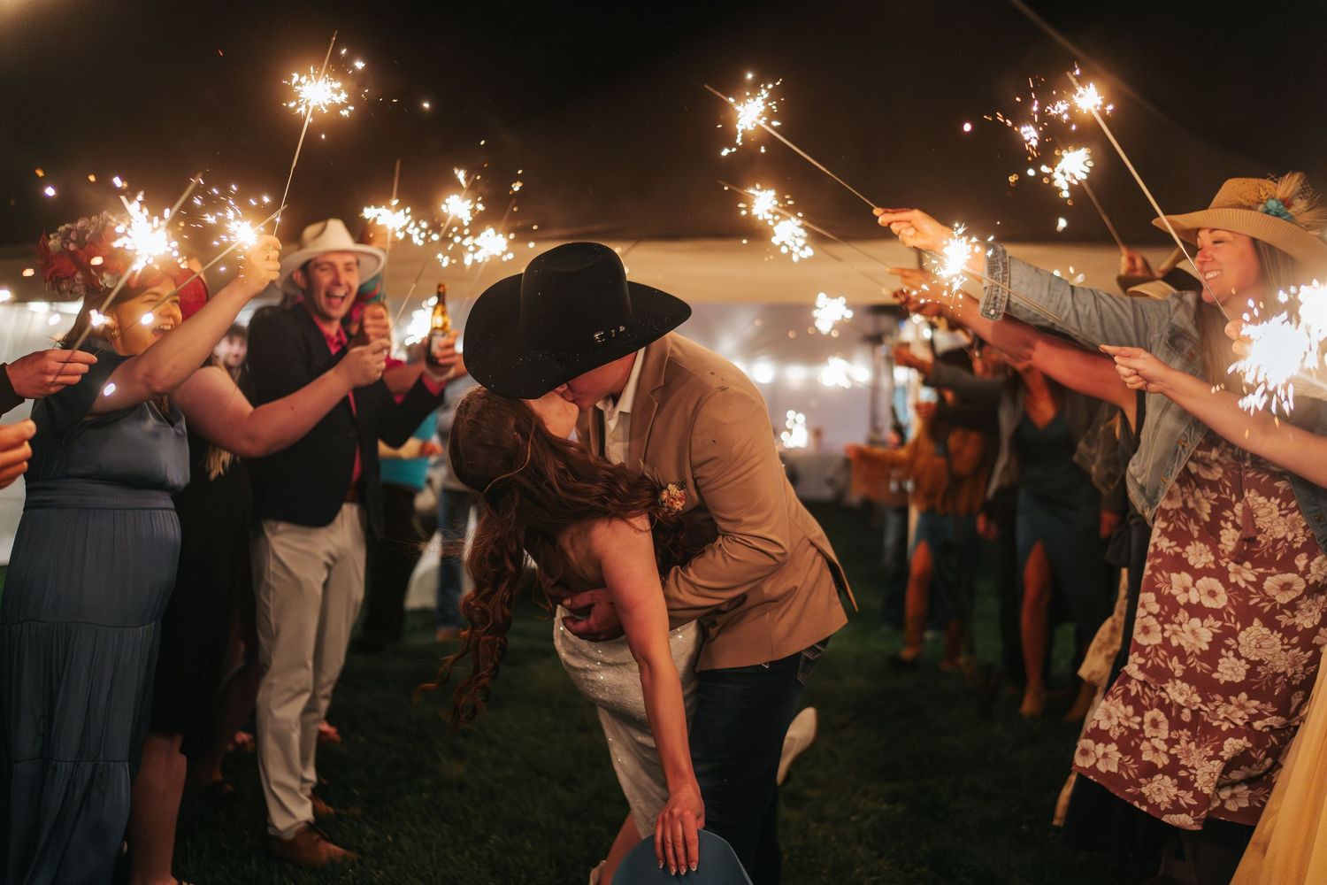Wedding guests celebrate with sparklers at night during an outdoor reception celebration.