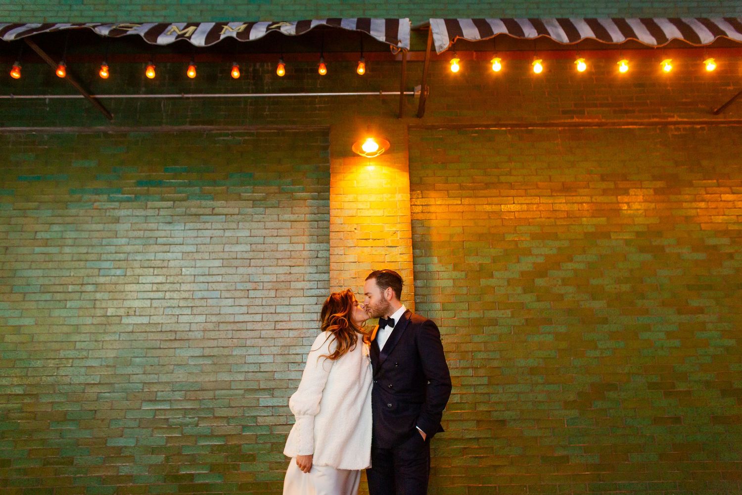 Romantic evening portraits with string lights creating warm ambiance against industrial brick backdrop.