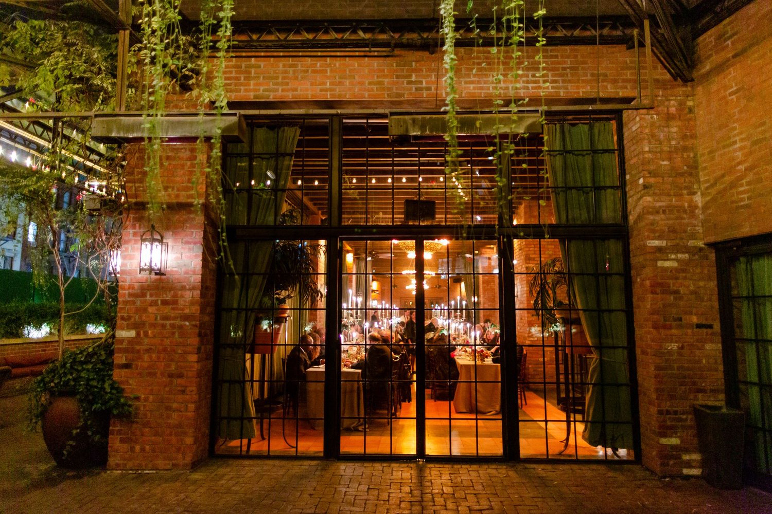 Historic brick warehouse building with industrial-style windows and string lights creates a warm, rustic ambiance.