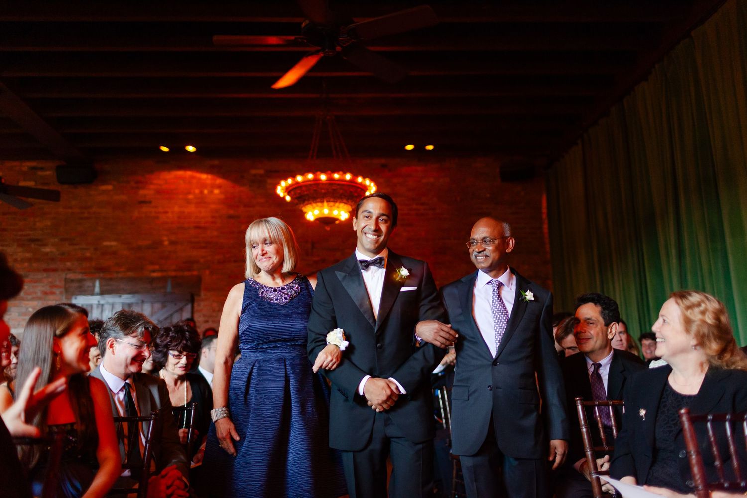 A row of wedding guests dancing and celebrating in a dimly lit reception hall with red and green lighting.