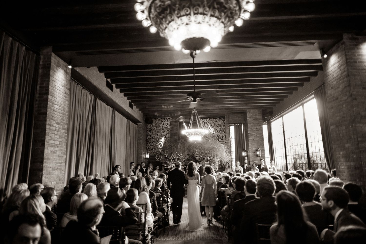Wedding guests dance and celebrate under elegant crystal chandeliers in a rustic reception venue.