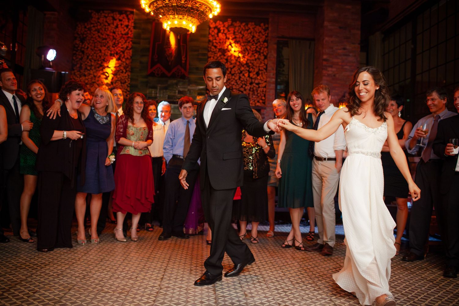 Wedding guests dance and celebrate on a dimly lit ballroom dance floor during an evening reception.