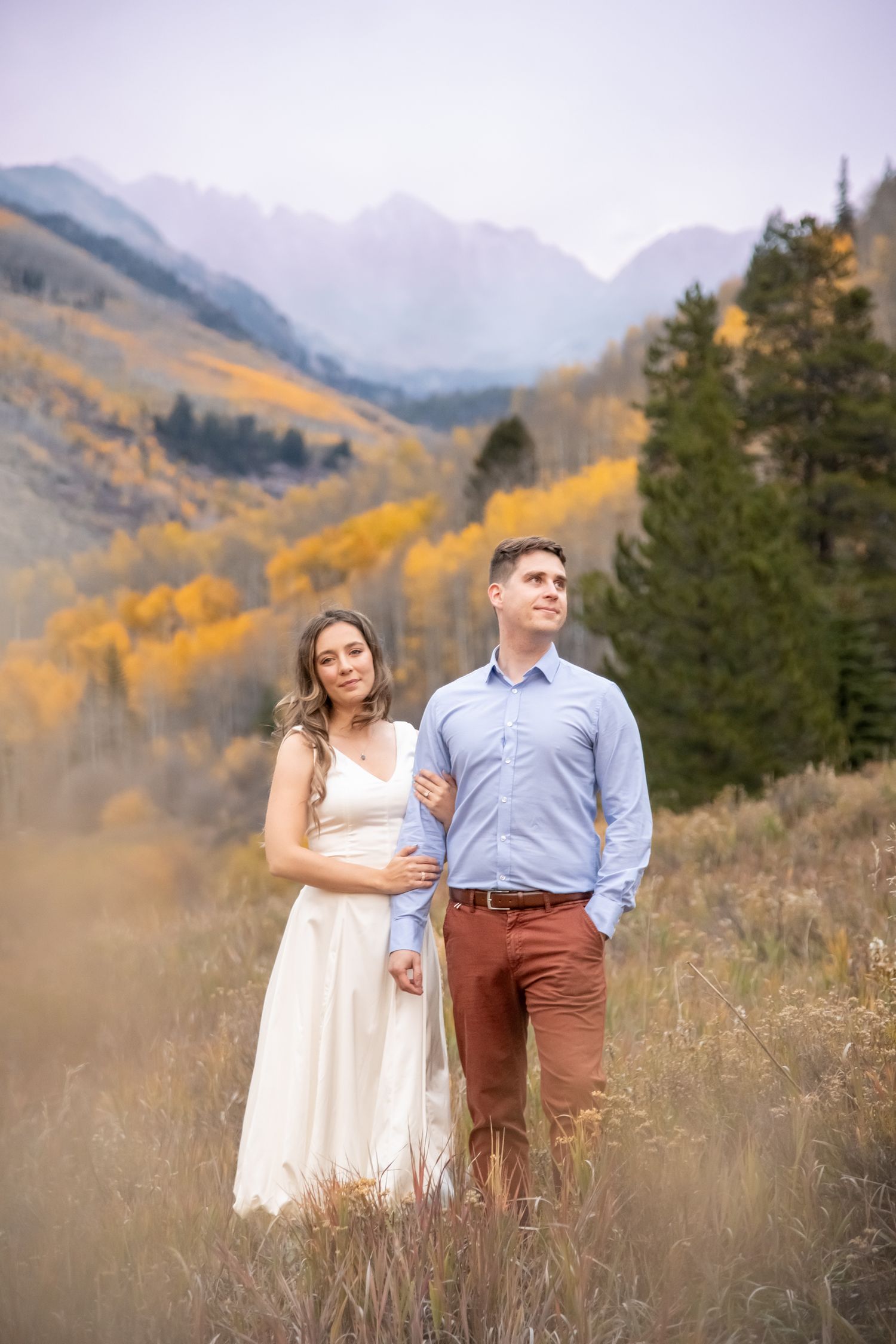 Vail engagement photos in a mountain meadow surrounded by golden autumn foliage and evergreen trees.