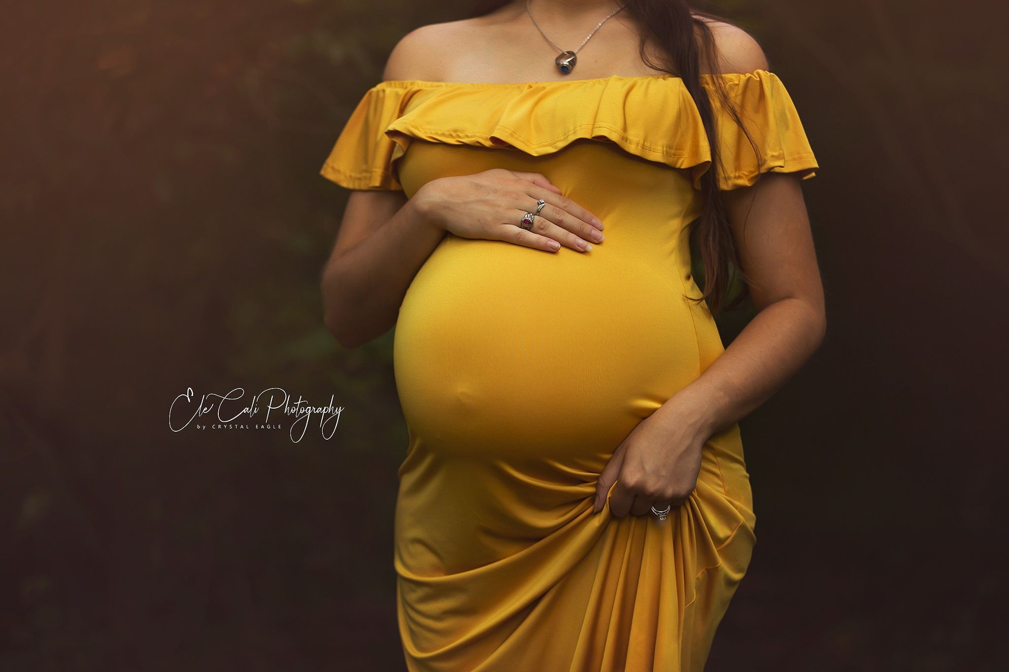 A maternity portrait featuring a yellow off-shoulder dress against a dark background.