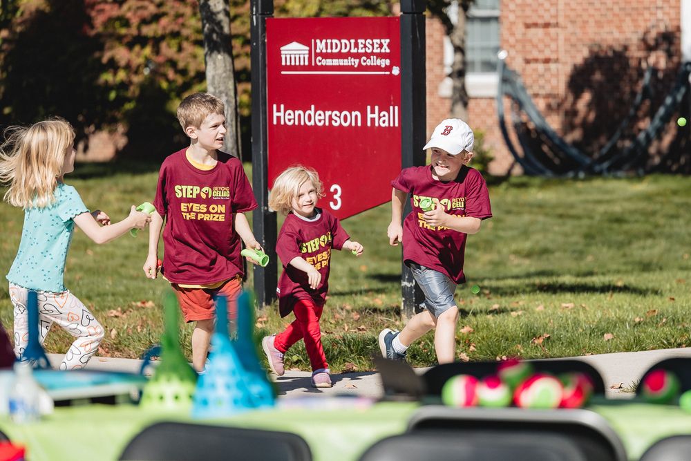 Students enjoy outdoor activities and games on a sunny day at a college campus with red banners visible in the background.