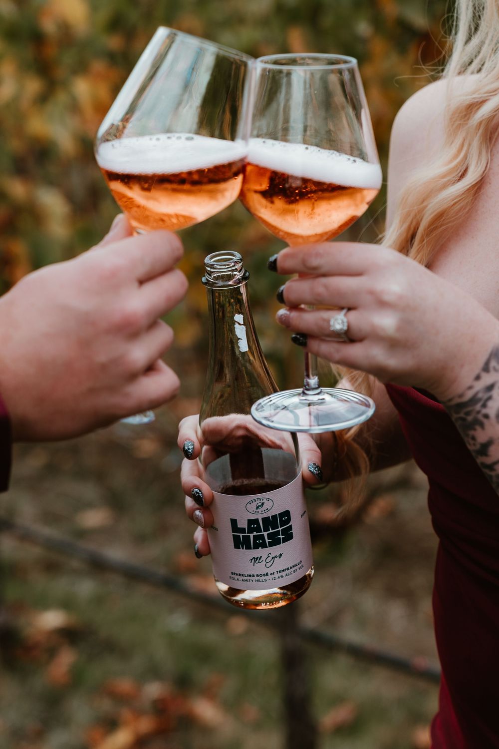 Couple toasting with glasses of rose wine holding a Landmass wine bottle in a vineyard.