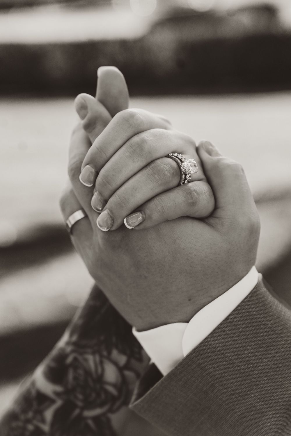 Close-up of newlyweds holding hands showing diamond engagement ring and wedding bands, black and white.
