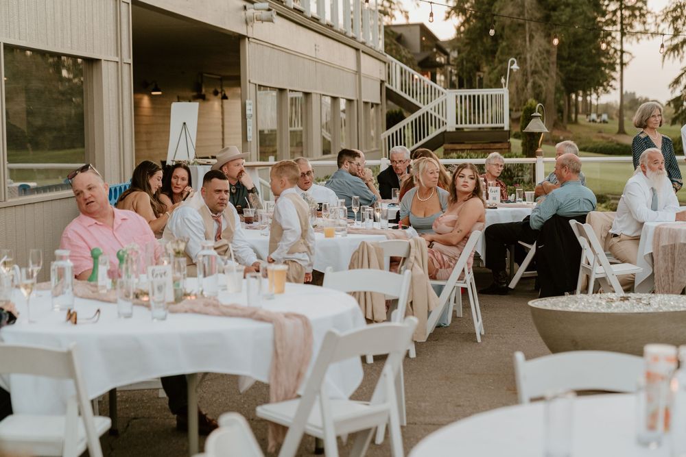 Wedding guests seated at white-clothed reception tables during outdoor evening wedding celebration.
