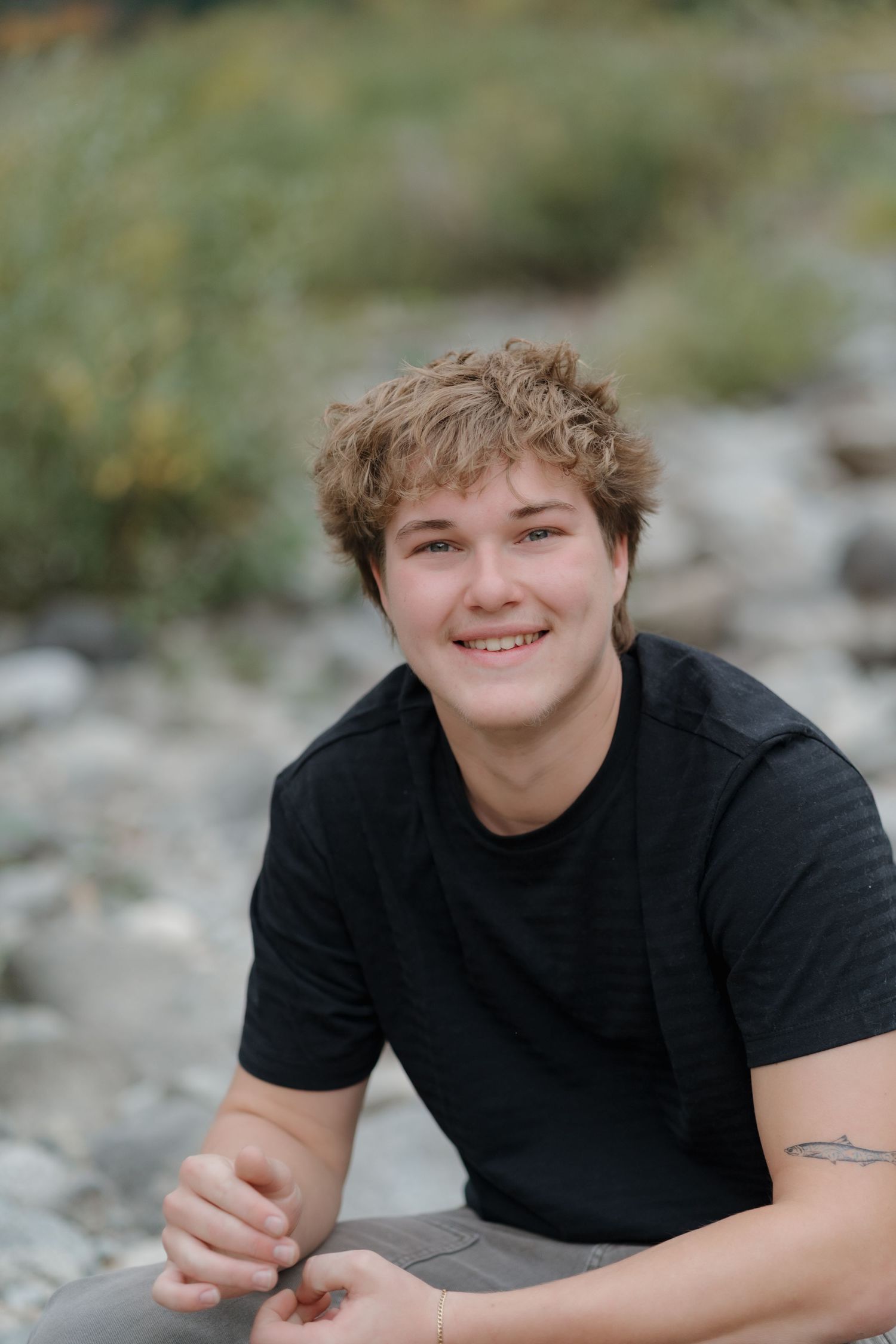 A casual outdoor portrait session by a river with natural lighting and rocky terrain.