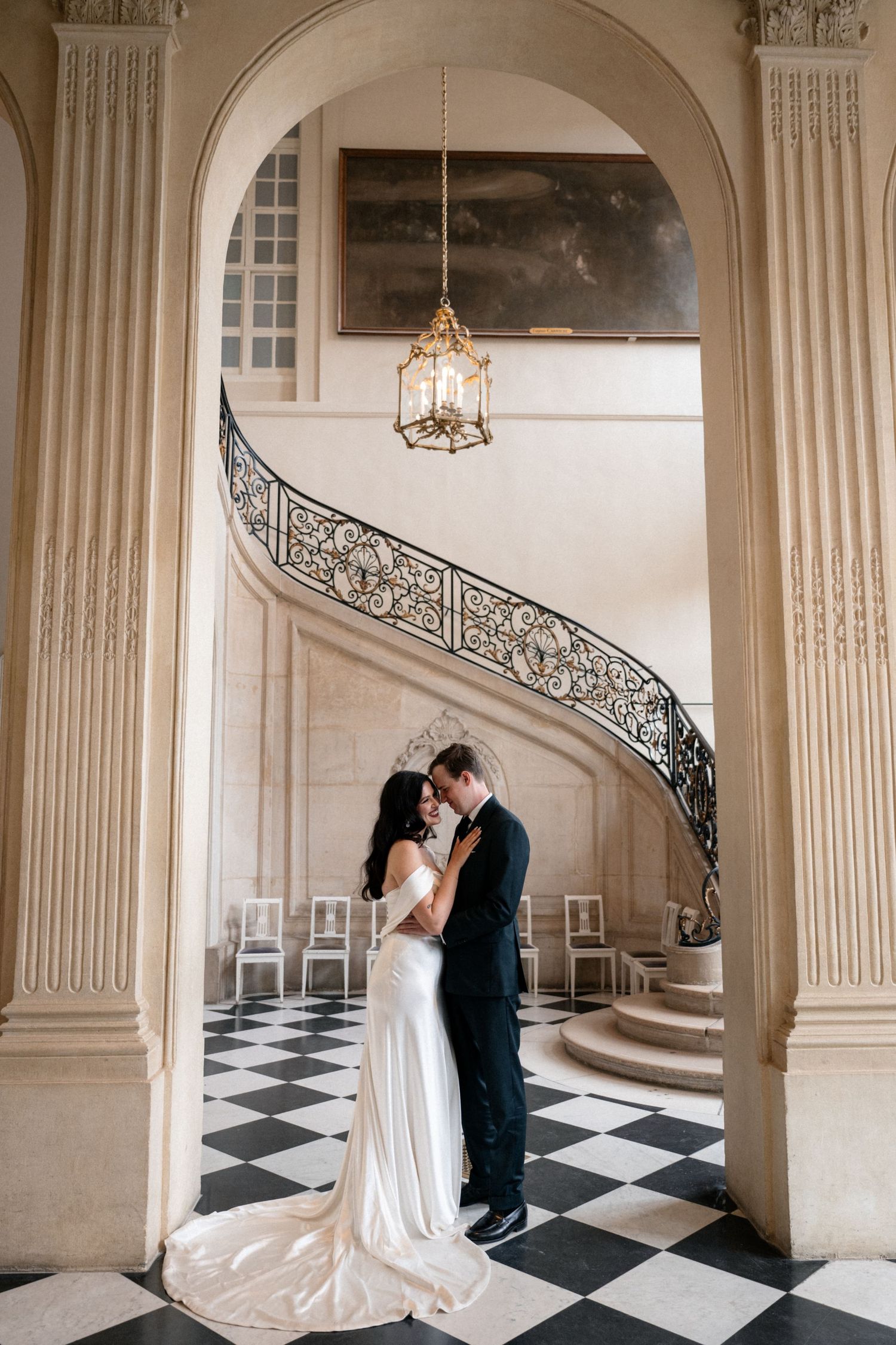 Elegant wedding couple shares romantic moments in a grand marble foyer with black and white checkered floors and arched columns.