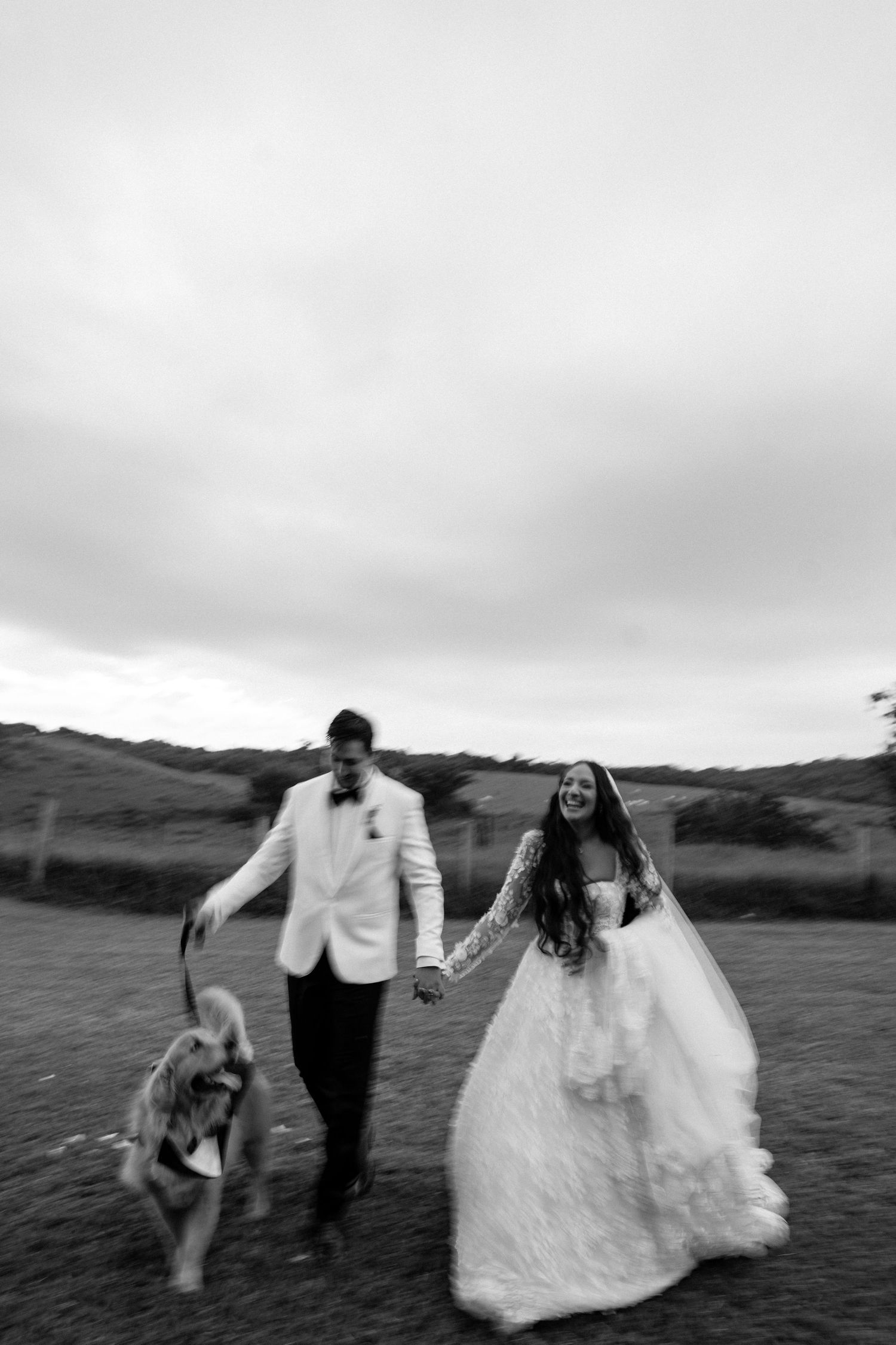 A bride in a white wedding dress smiles joyfully during an outdoor wedding ceremony.