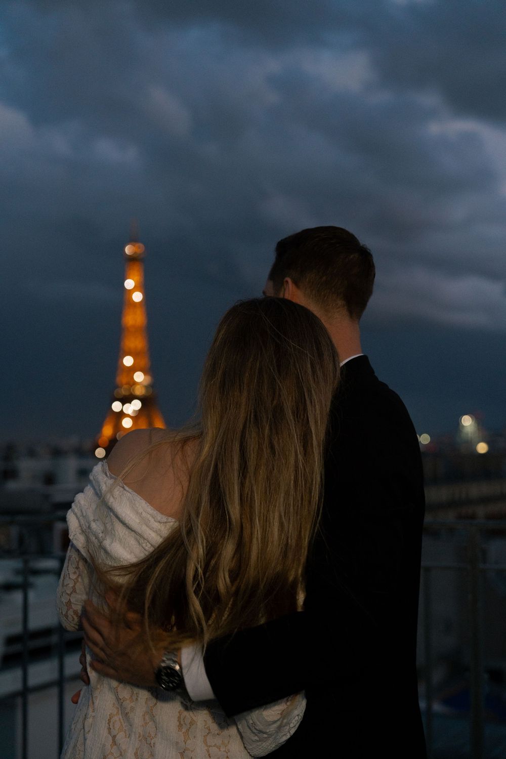 A couple shares a romantic moment at dusk with city lights glowing in the background.