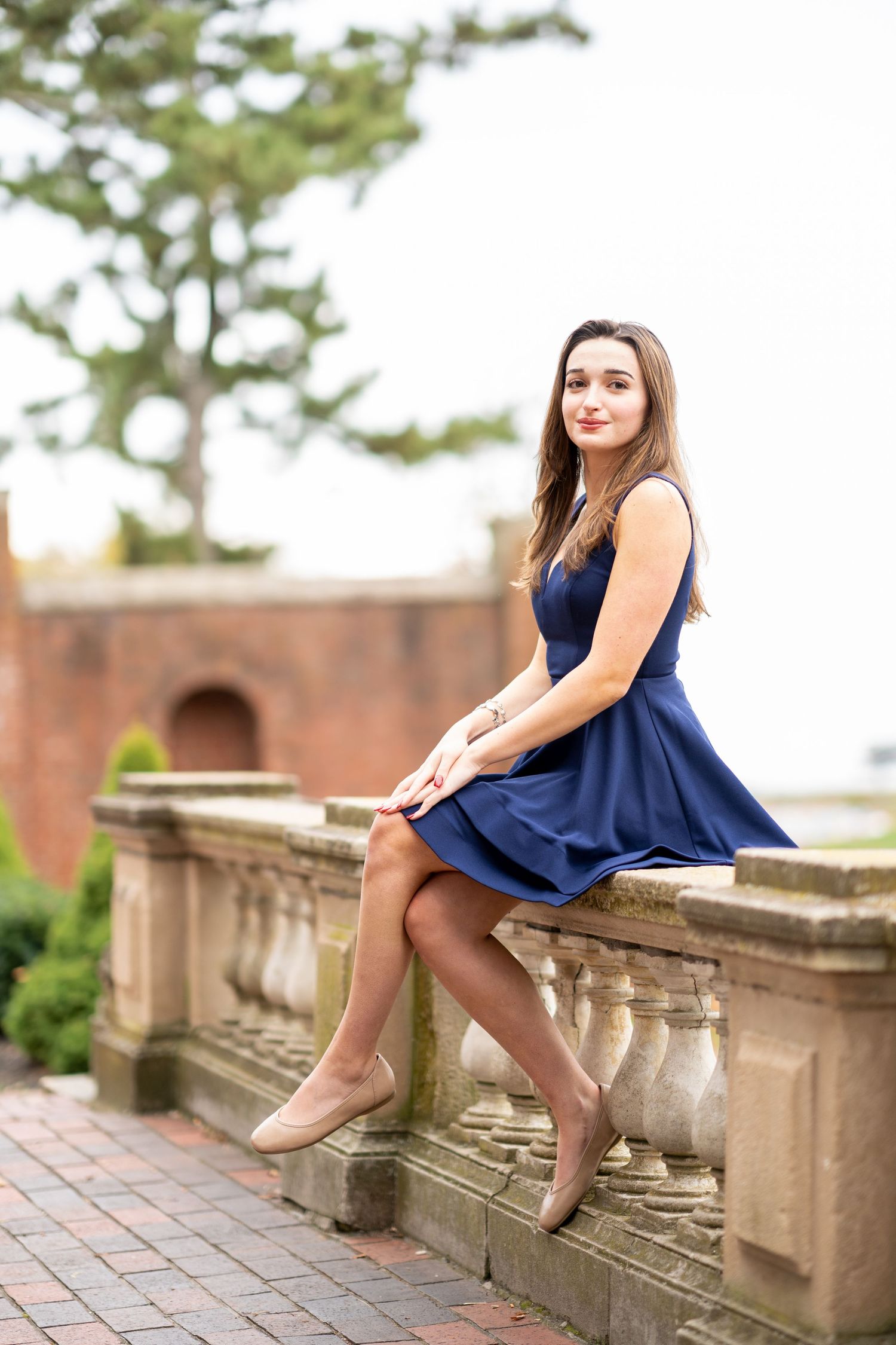 A person in a navy blue dress poses gracefully on stone steps in an outdoor portrait session.
