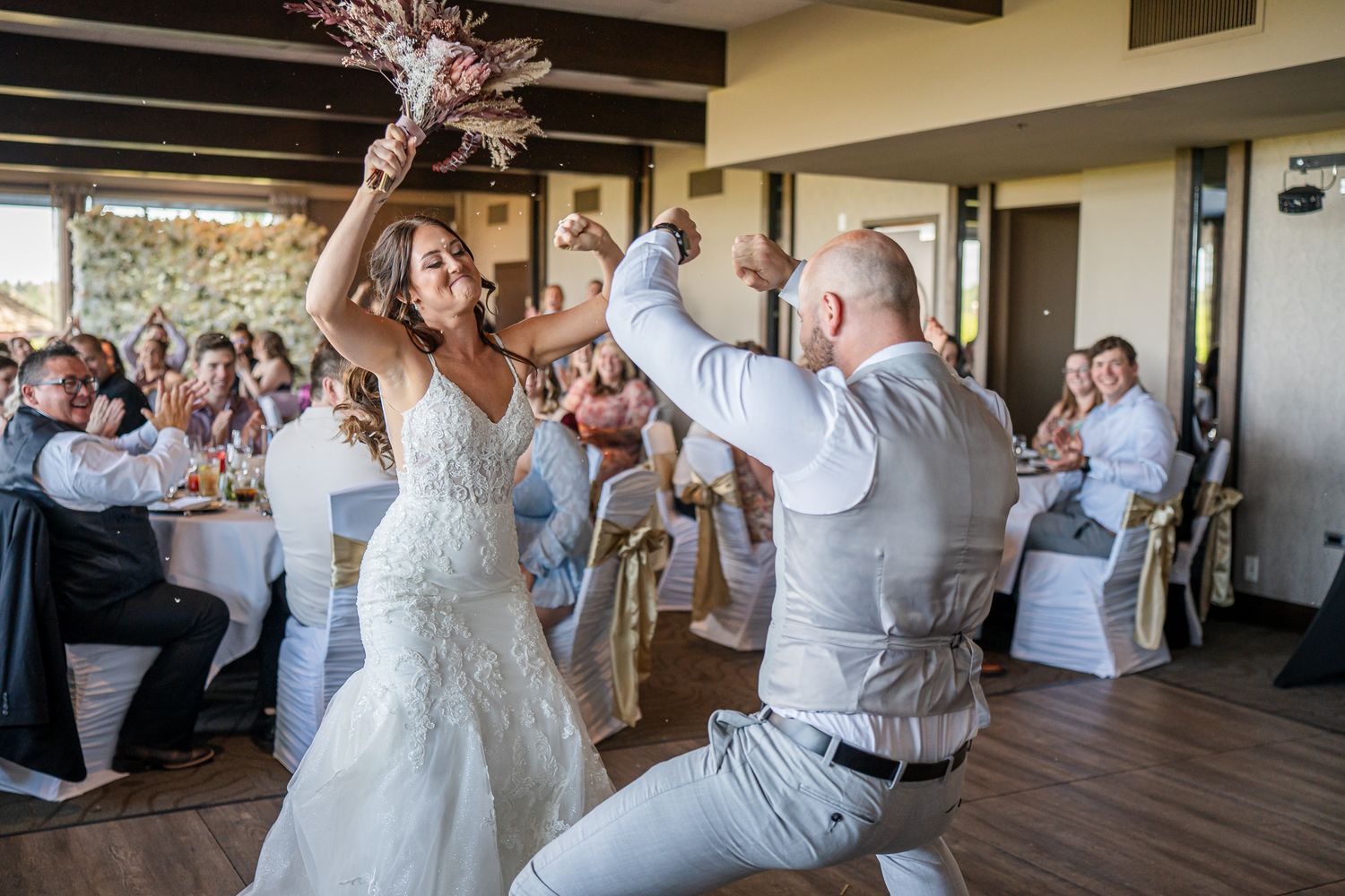 Wedding guests dance and celebrate together on a wooden dance floor at an indoor reception venue.