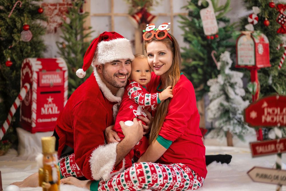 Christmas photo with matching red holiday pajamas and Santa hat in front of festive mailbox and snowy decor.