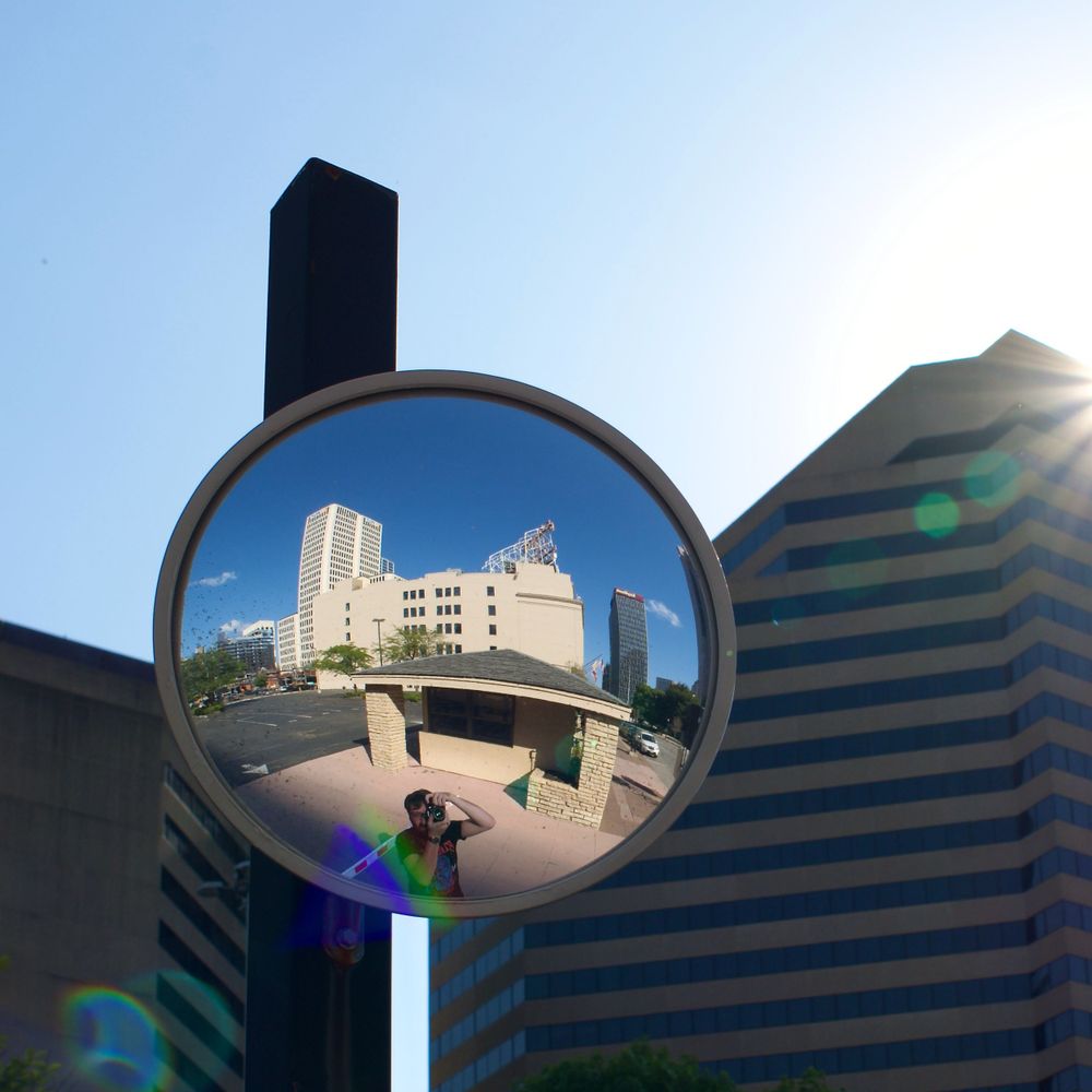 Convex security mirror reflects modern urban buildings against blue sky.