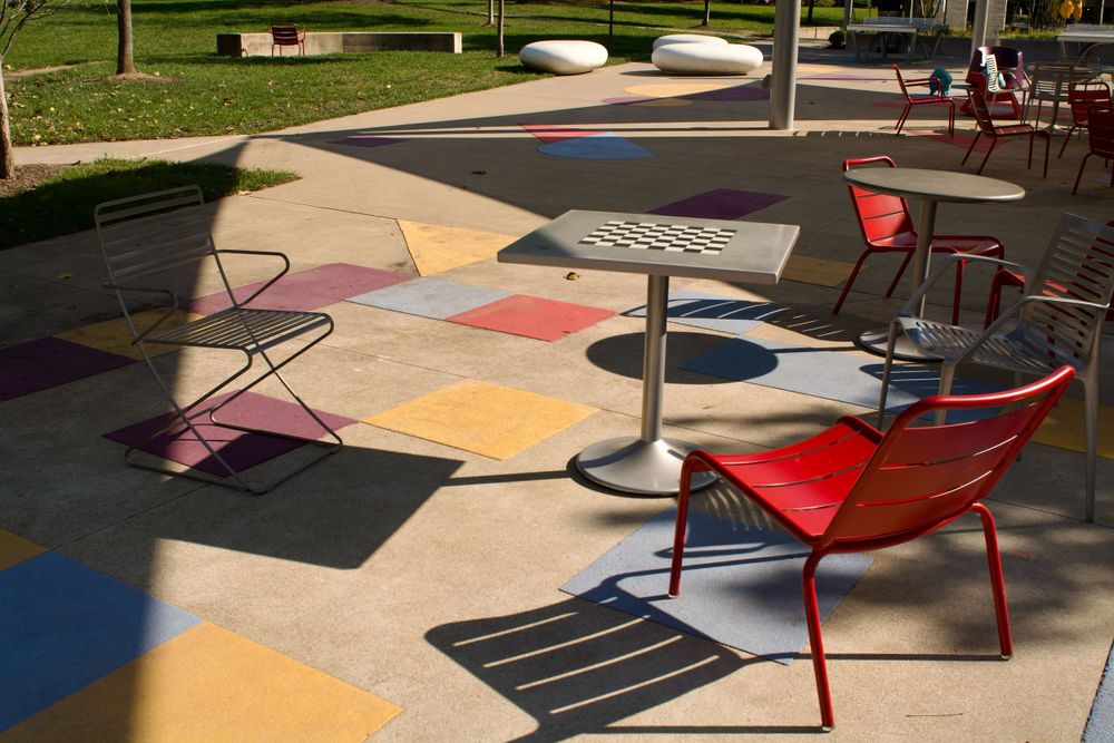 Colorful geometric patio setup with red chairs and round table on painted concrete.