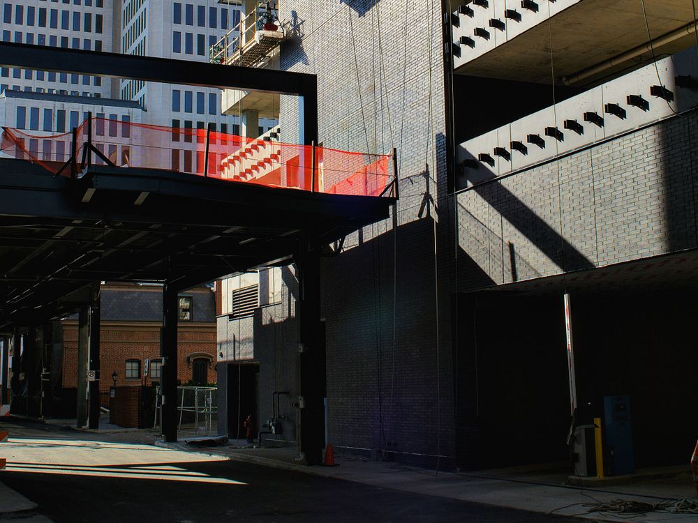Urban street scene with red architectural element and strong shadows between buildings.