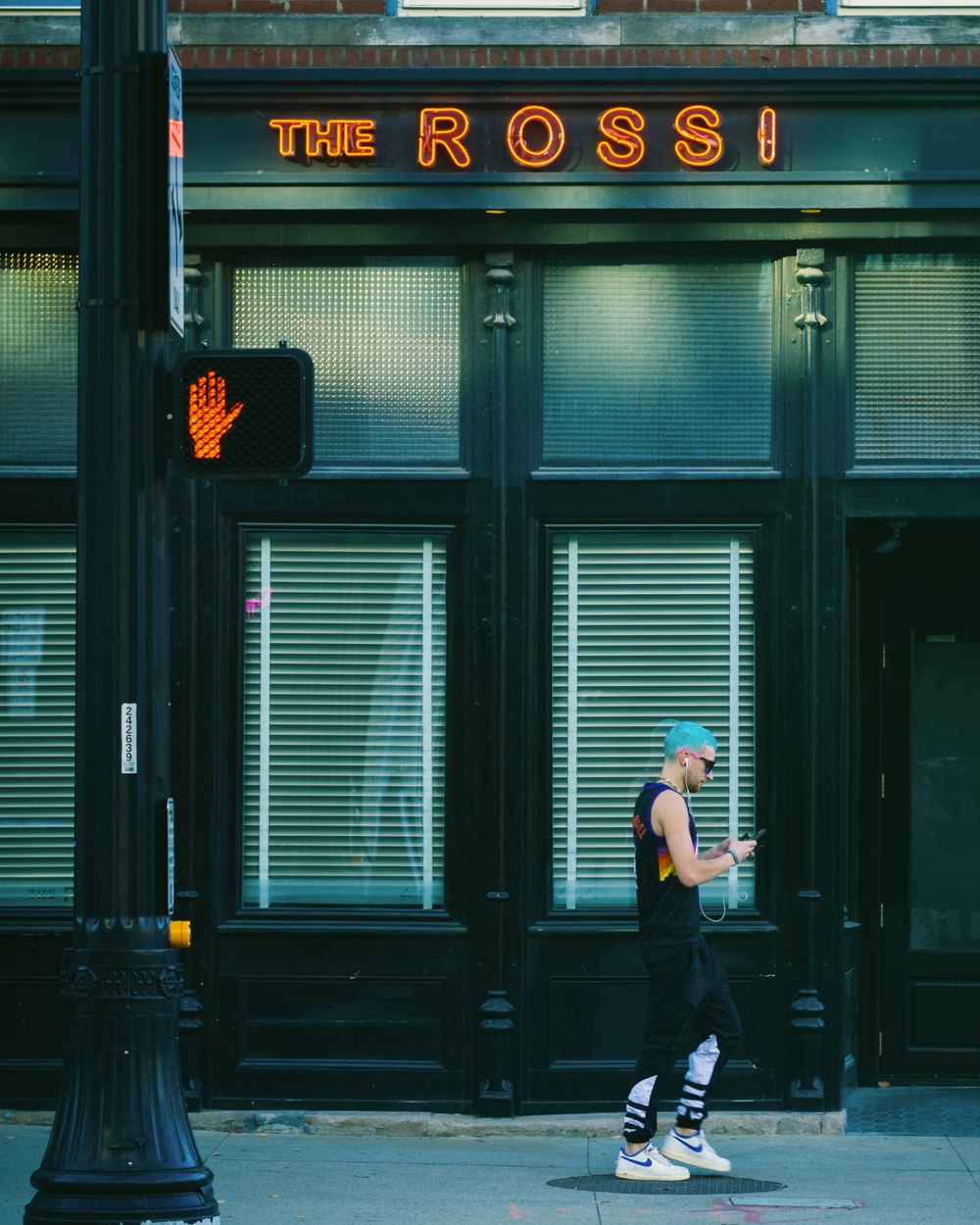 Neon sign reading 'The Rossi' glows above a storefront with a illuminated hand symbol.