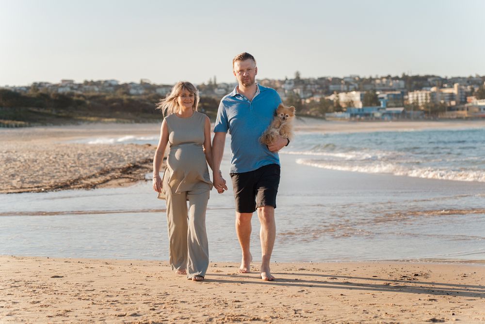 couple walking together on a sandy beach at sunset with ocean waves in the background during their maternity photoshoot in Sydney