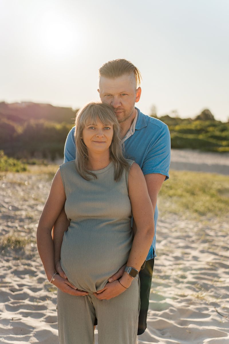 A couple hugging on a sunny beach during a romantic sunset maternity photoshoot in Sydney
