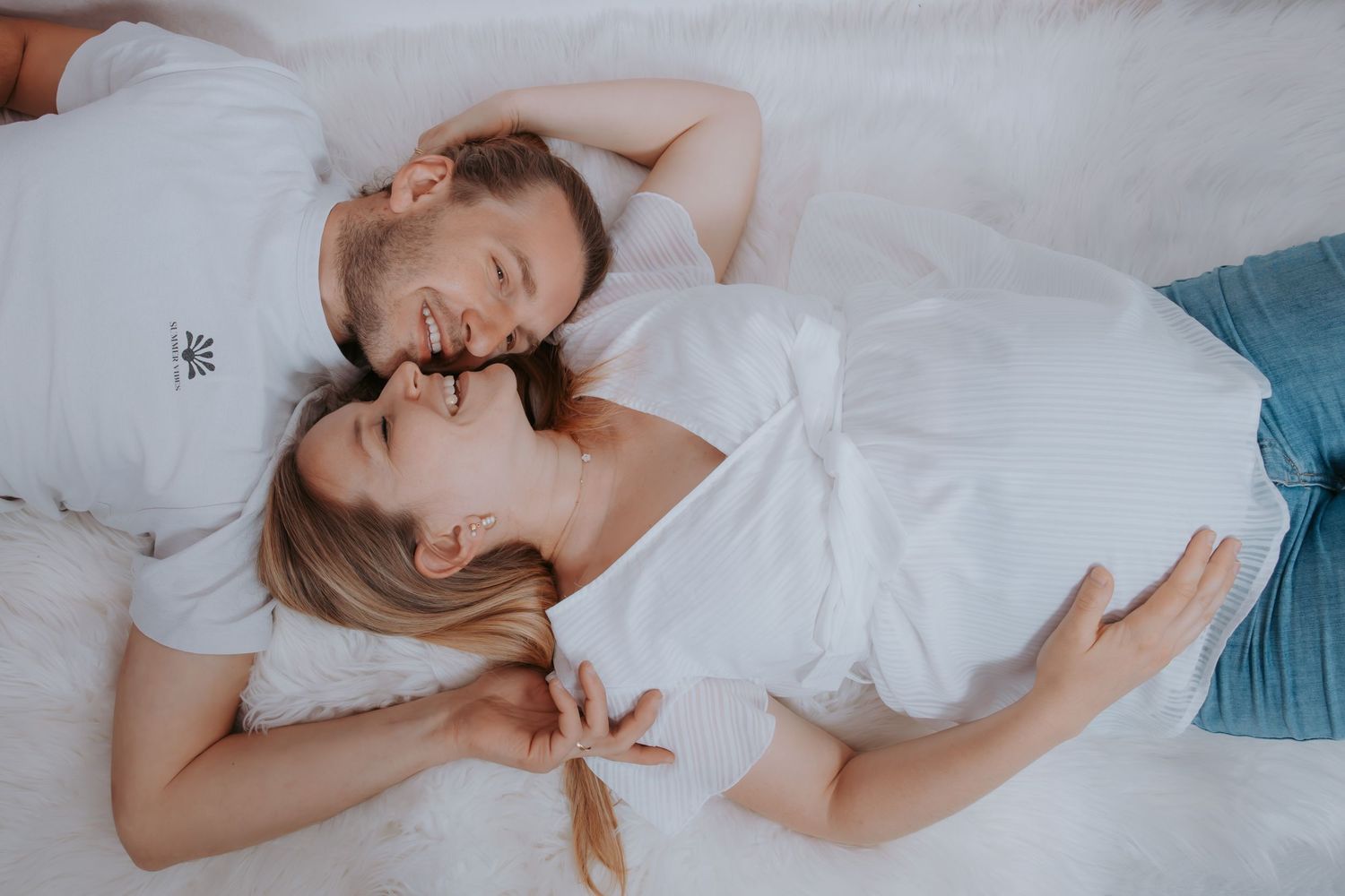 Couple lying down together on white bedding in soft natural light.