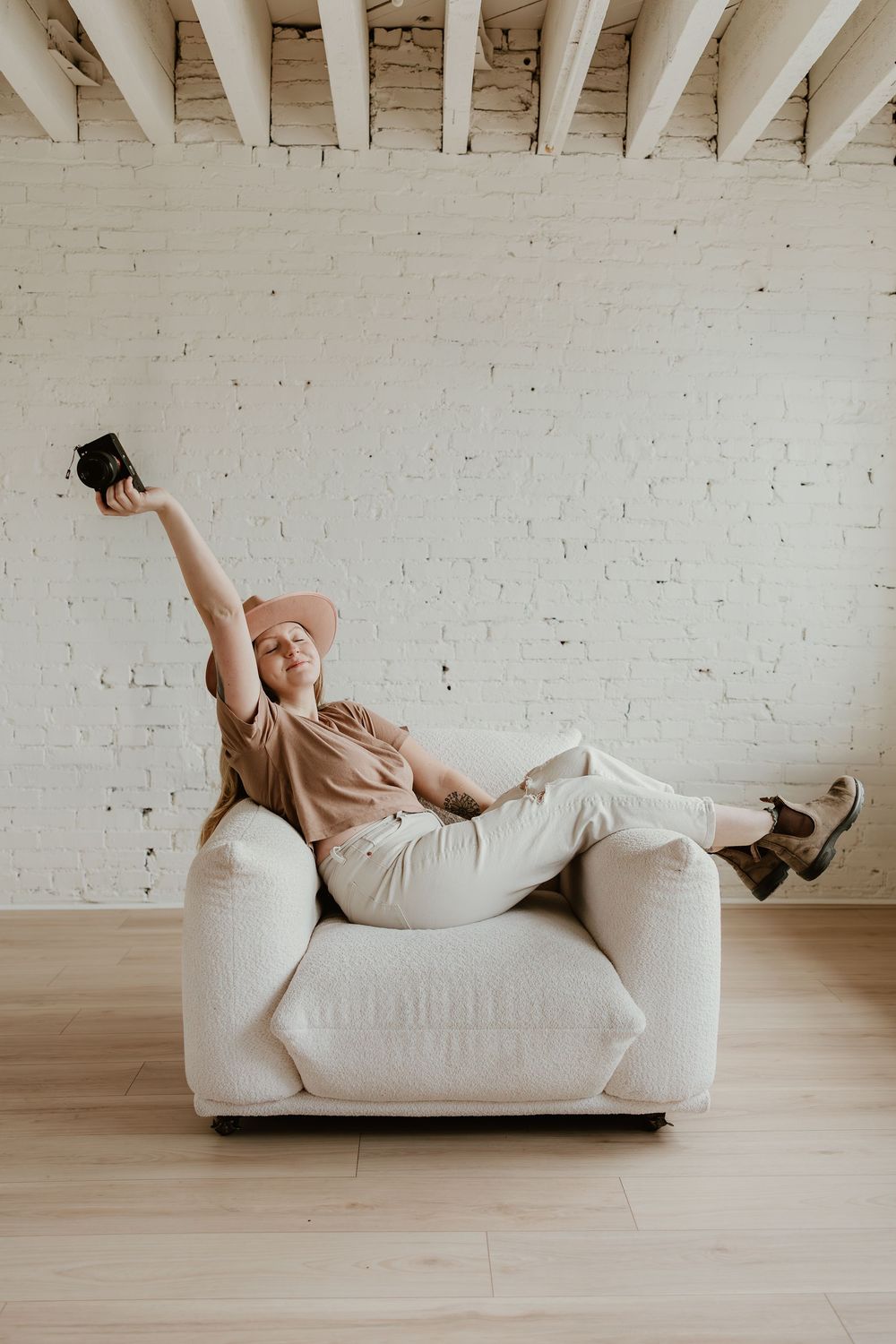 A person in casual attire lounges playfully across a white couch in a minimalist room with white brick walls.