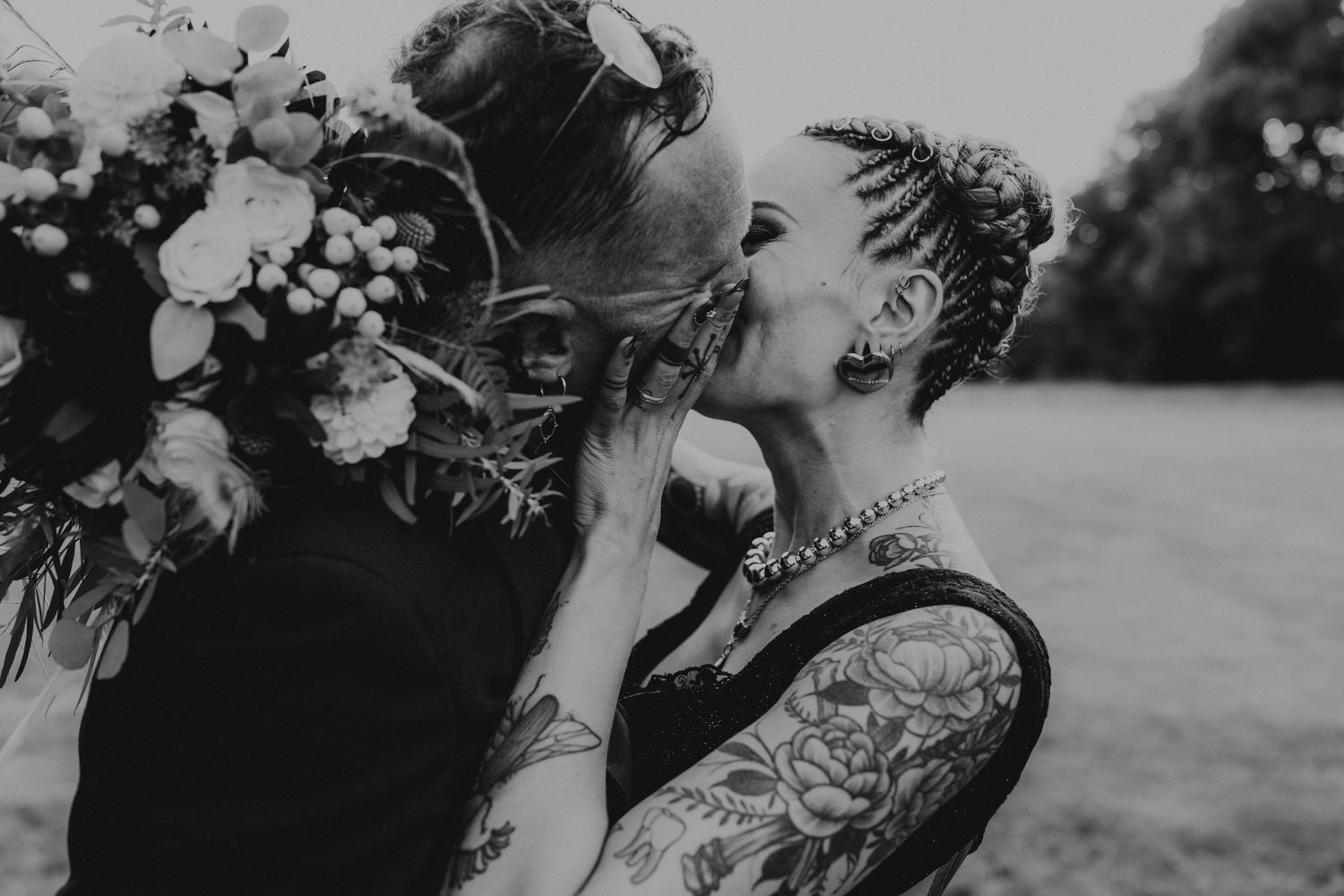 A romantic black and white wedding photograph showing a tender embrace in a natural outdoor setting.